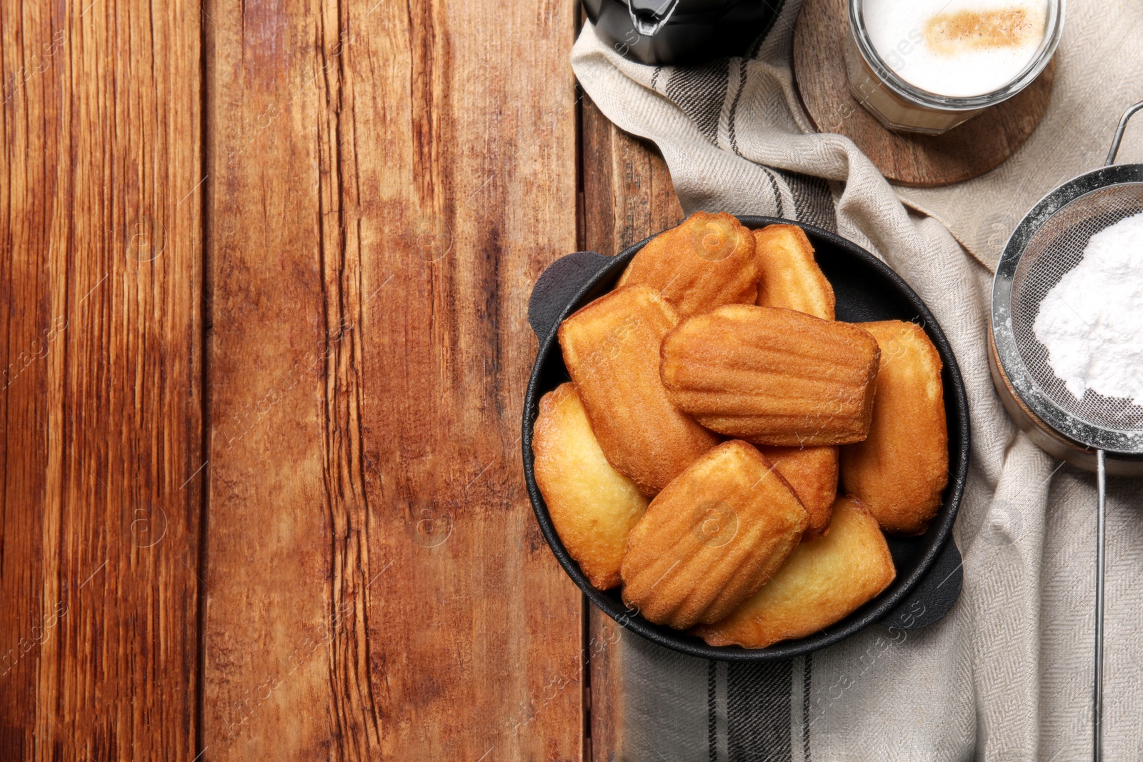 Photo of Delicious madeleine cakes, powdered sugar and coffee on wooden table, flat lay Space for text