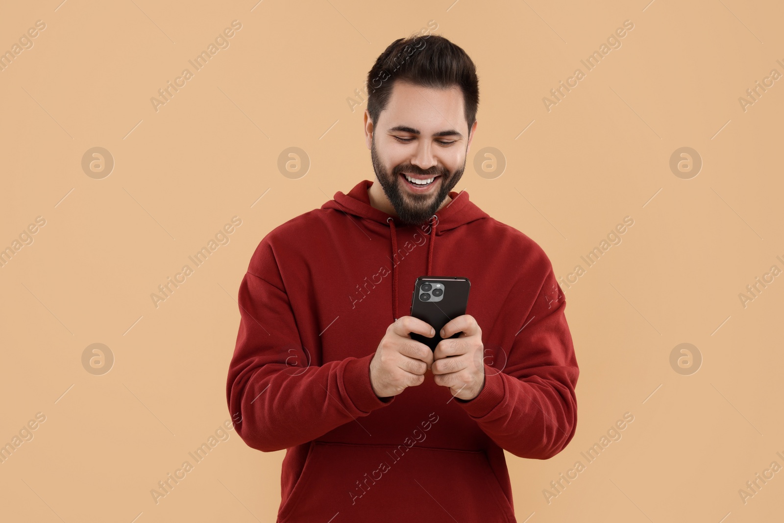 Photo of Happy young man using smartphone on beige background