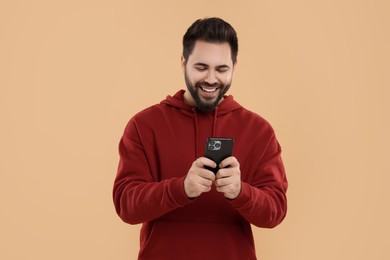 Photo of Happy young man using smartphone on beige background