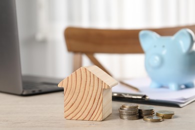 Photo of House model, coins, piggy bank and laptop on wooden table indoors, selective focus