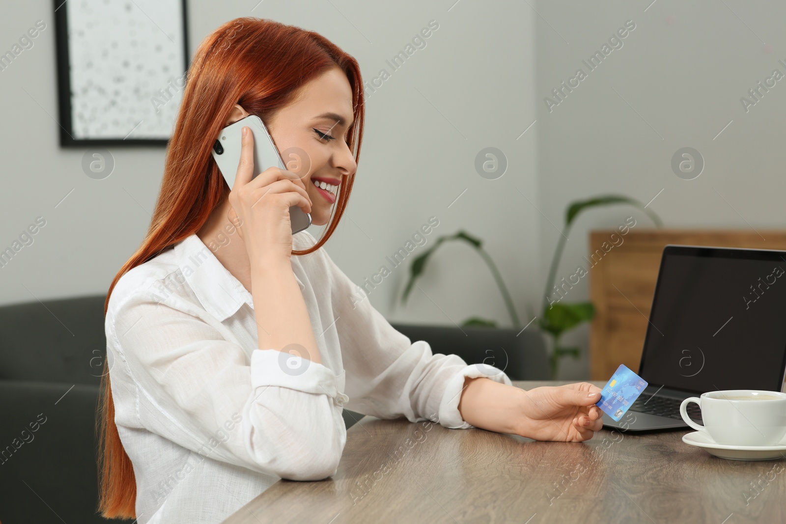 Photo of Happy woman with credit card using smartphone for online shopping at wooden table in room. Space for text