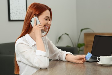 Photo of Happy woman with credit card using smartphone for online shopping at wooden table in room. Space for text