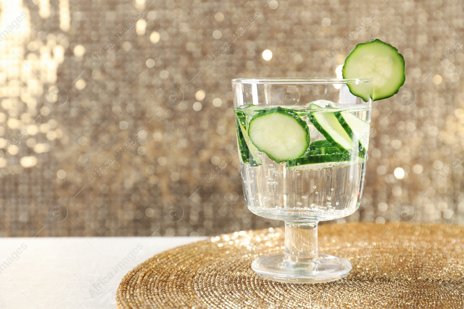 Photo of Glass of fresh cucumber water on golden mat. Space for text