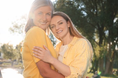Photo of Family portrait of happy mother and daughter hugging outdoors on sunny day