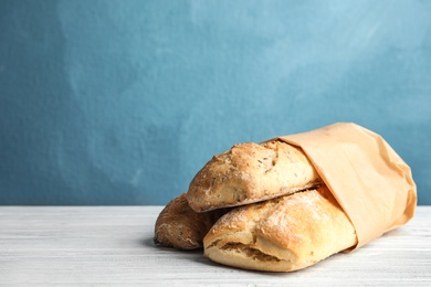 Photo of Mini baguettes in paper bag on table against color background, space for text. Wholegrain bread
