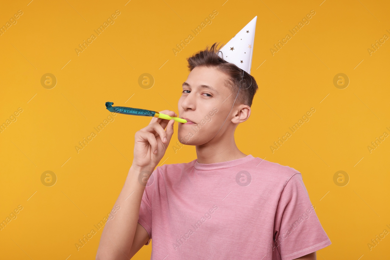 Photo of Young man in party hat with blower on orange background