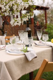 Photo of Stylish table setting with beautiful spring flowers, wine, plates and glasses in garden