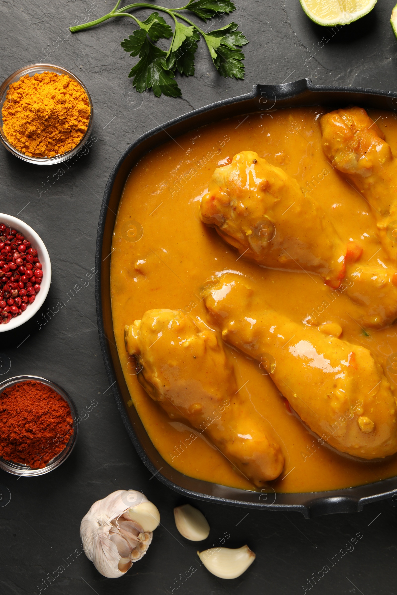 Photo of Tasty chicken curry and ingredients on black textured table, flat lay