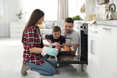 Photo of Woman and her family taking out tray with baked buns from oven in kitchen