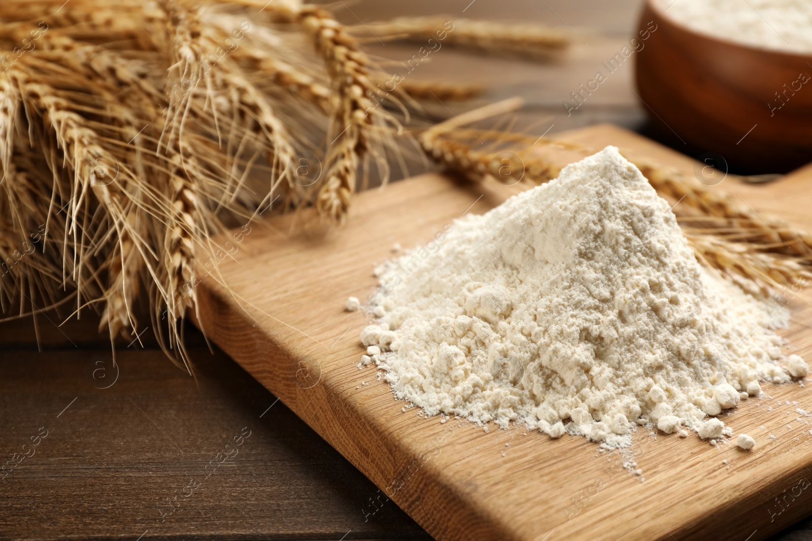 Photo of Pile of flour and wheat ears on wooden table, closeup