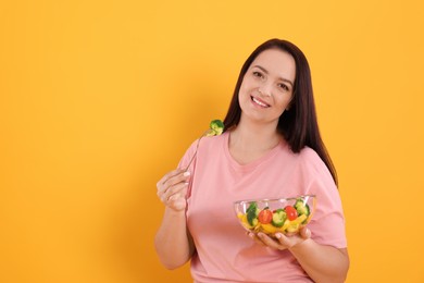 Photo of Beautiful overweight woman eating salad on yellow background, space for text. Healthy diet