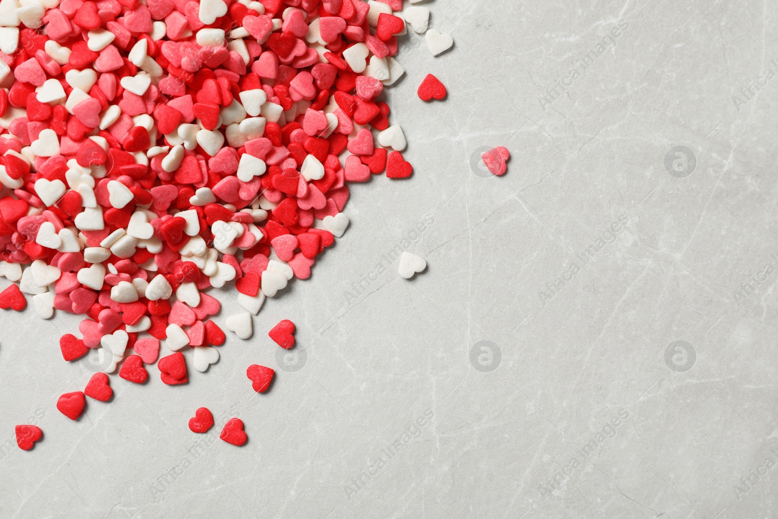 Photo of Bright heart shaped sprinkles on light grey table, flat lay. Space for text