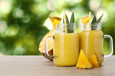 Image of Tasty pineapple smoothie in mason jars on wooden table against blurred background, space for text