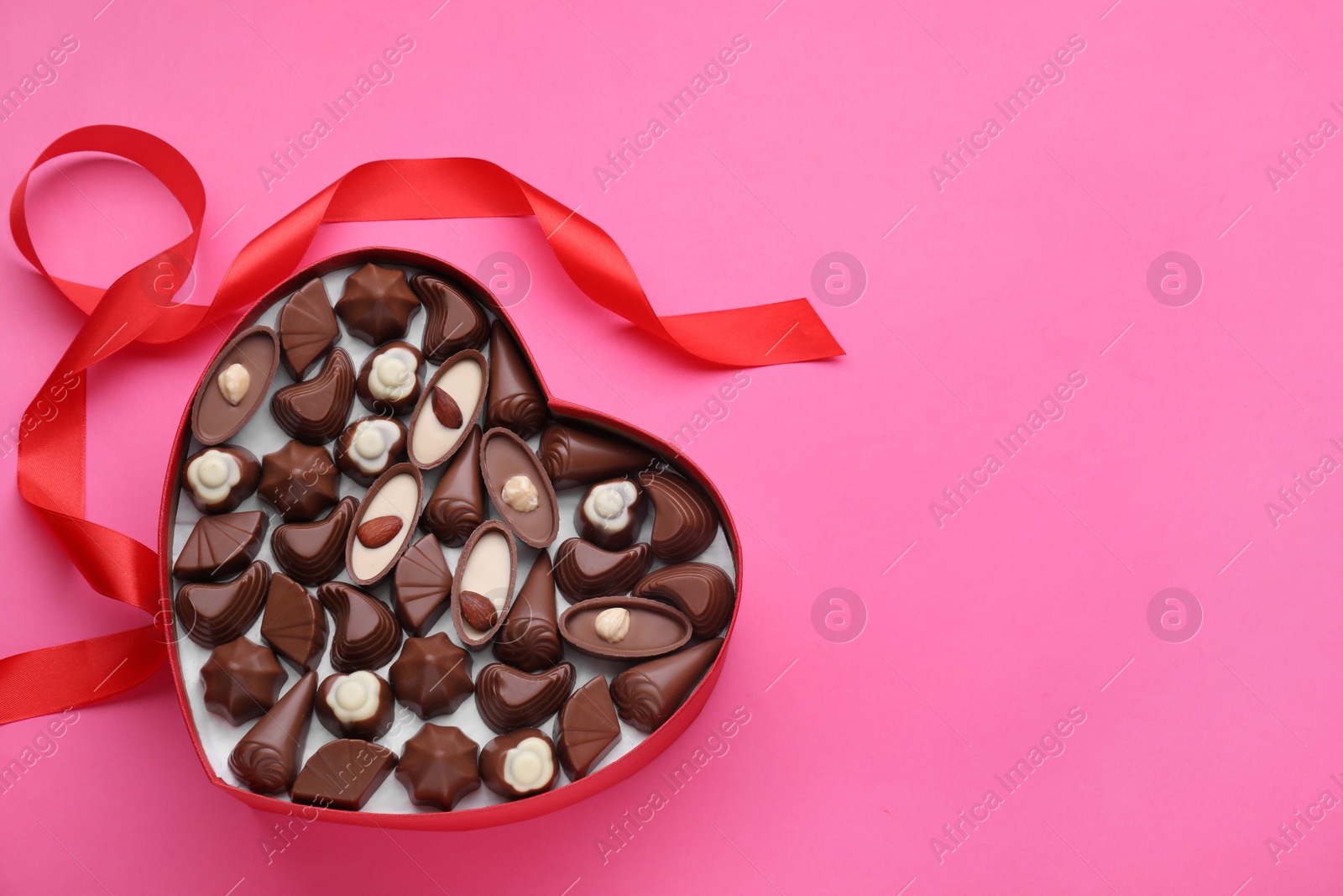 Photo of Heart shaped box with delicious chocolate candies and ribbon on pink background, flat lay. Space for text