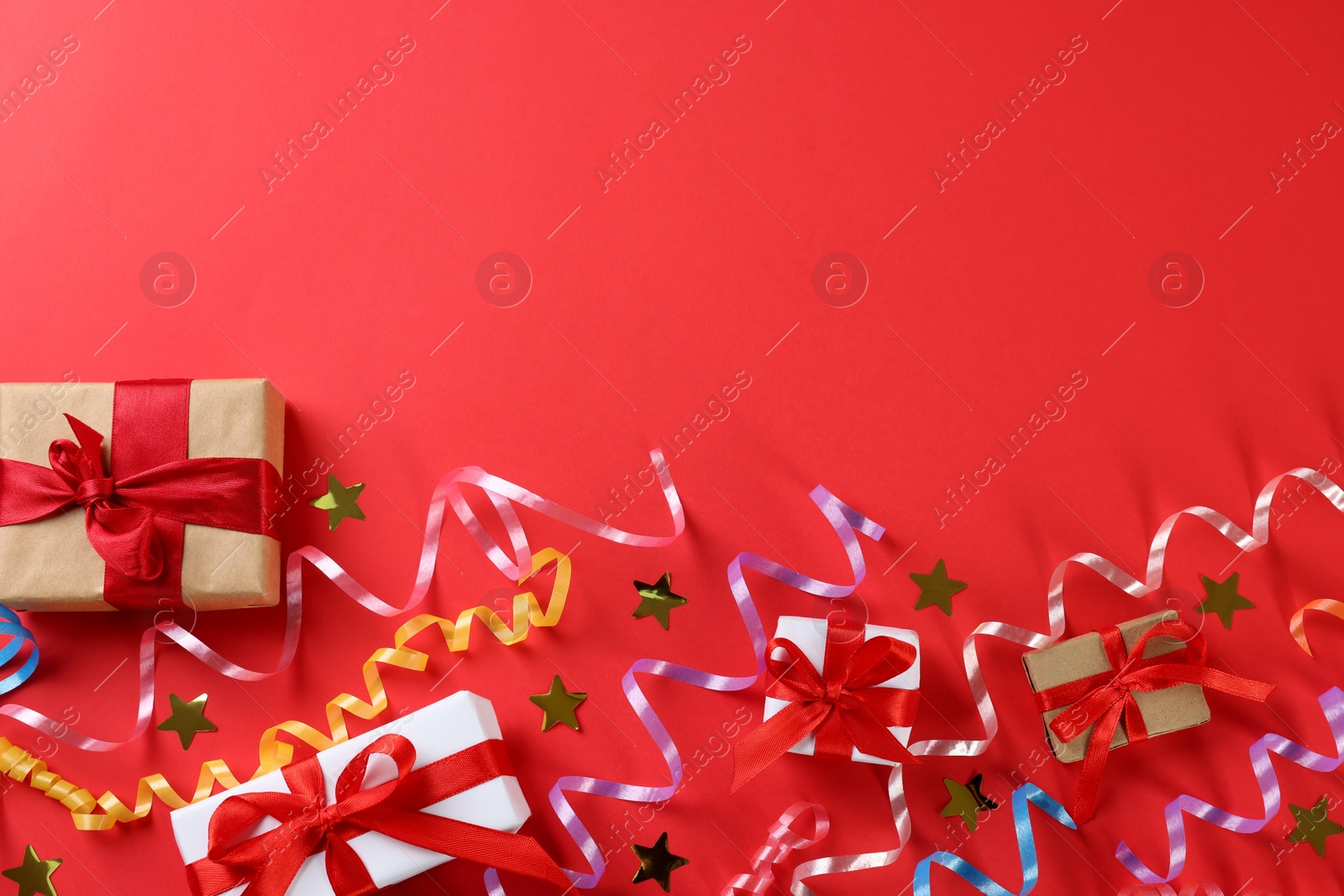 Photo of Colorful serpentine streamers, gift boxes and confetti on red background, flat lay. Space for text