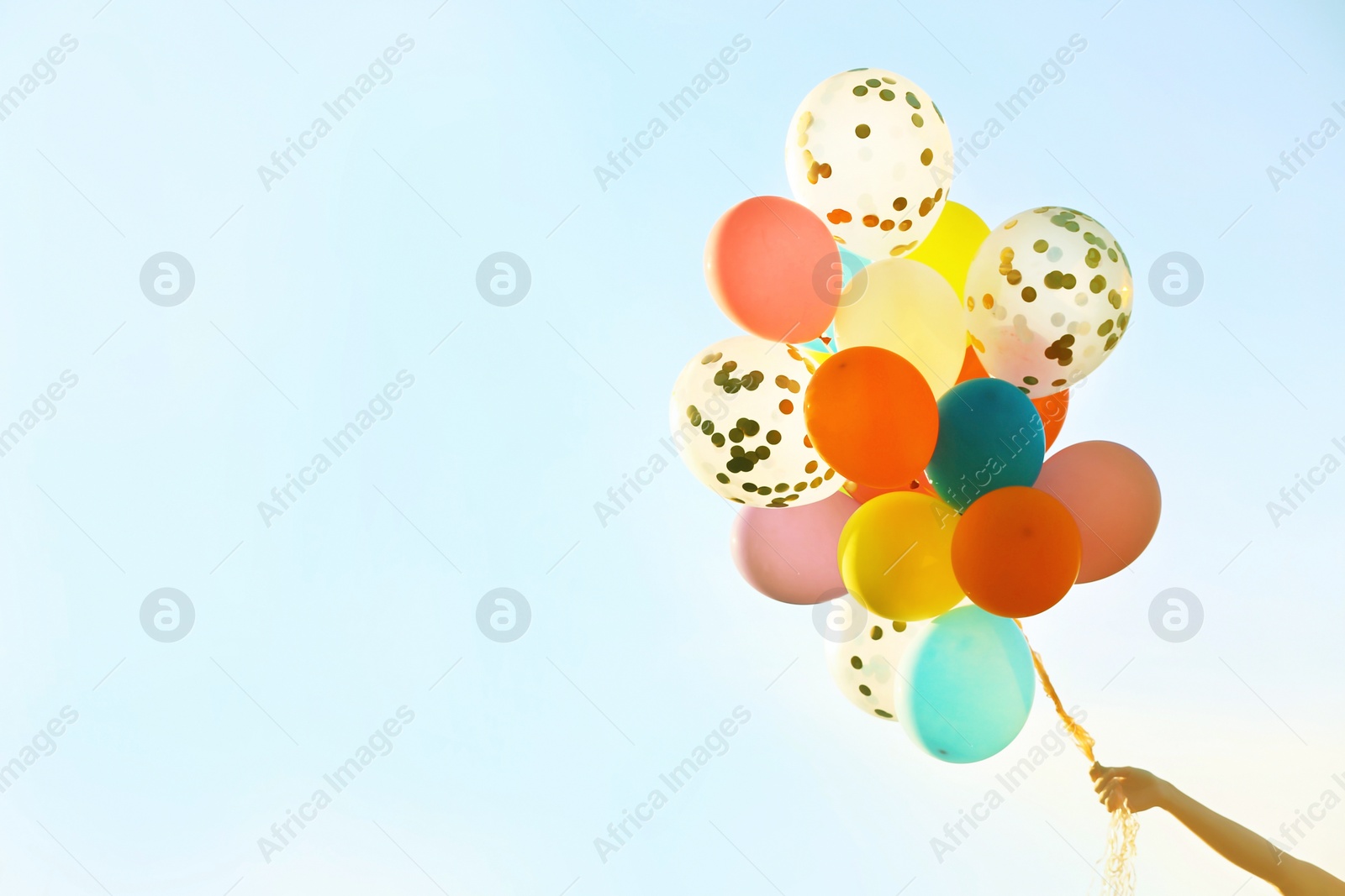 Image of Woman holding bunch of colorful balloons against sky, closeup. Space for text