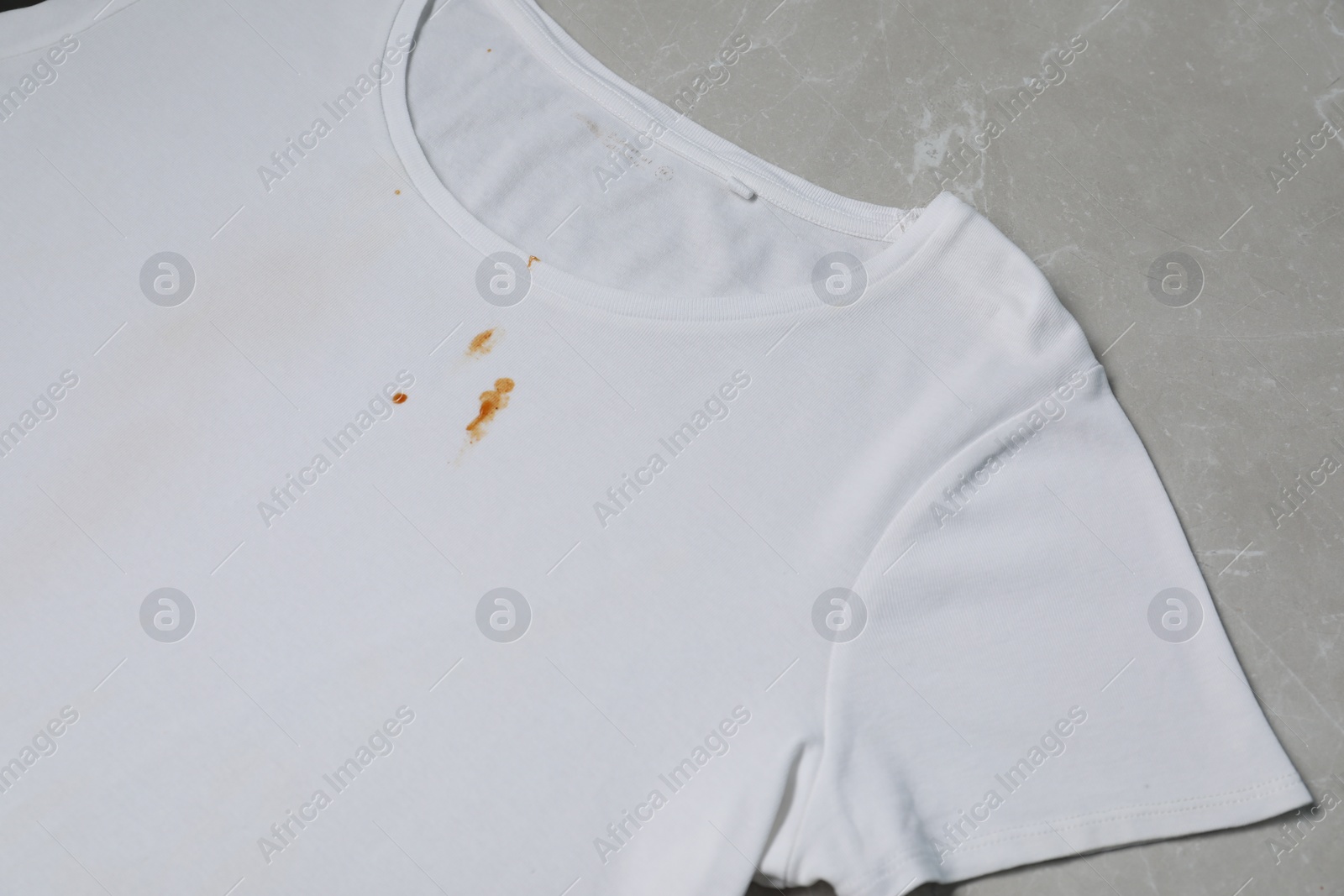 Photo of Dirty t-shirt with stains of sauce on light grey marble table, above view