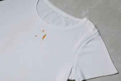 Photo of Dirty t-shirt with stains of sauce on light grey marble table, above view