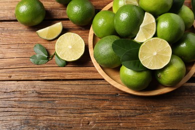 Photo of Fresh ripe limes and green leaves on wooden table, flat lay. Space for text