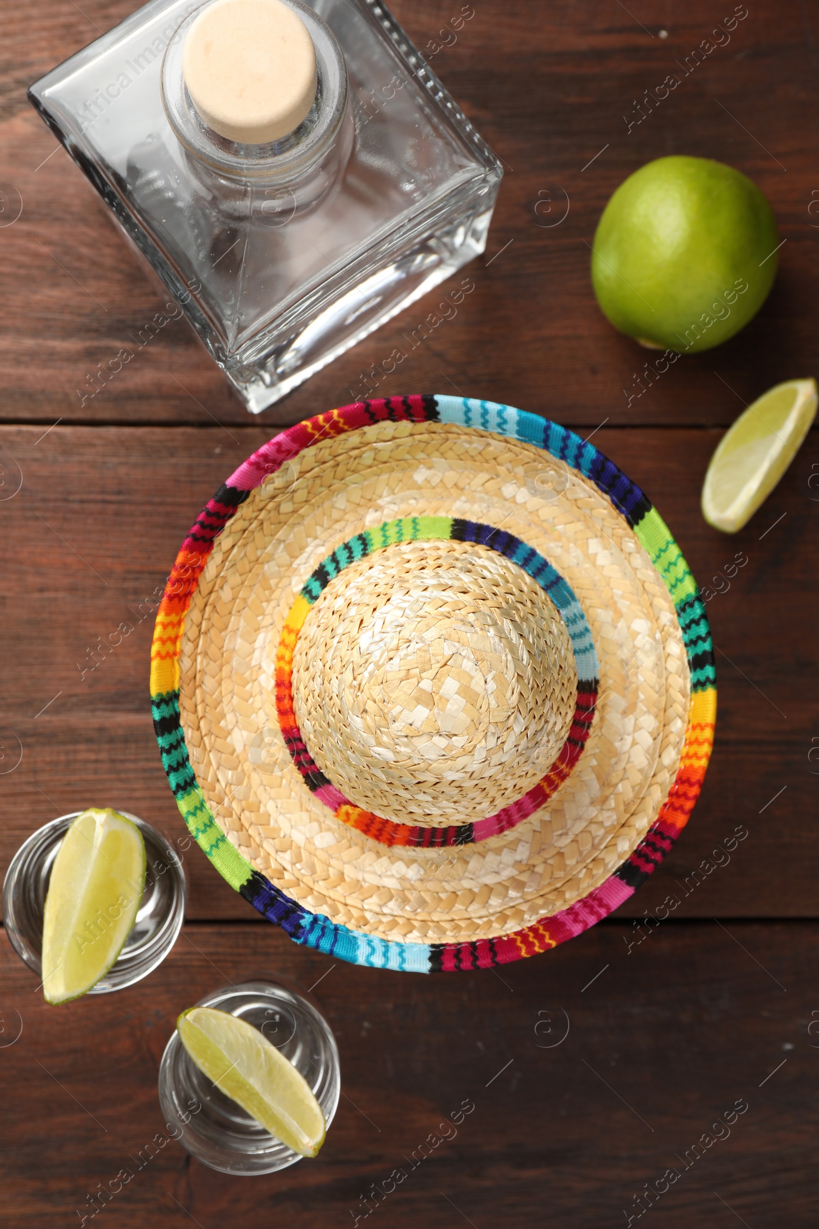 Photo of Mexican sombrero hat, tequila and lime on wooden table, flat lay