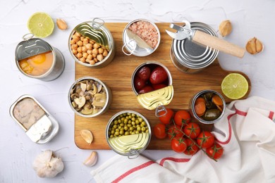 Photo of Open tin cans with different preserved products on white textured table, flat lay