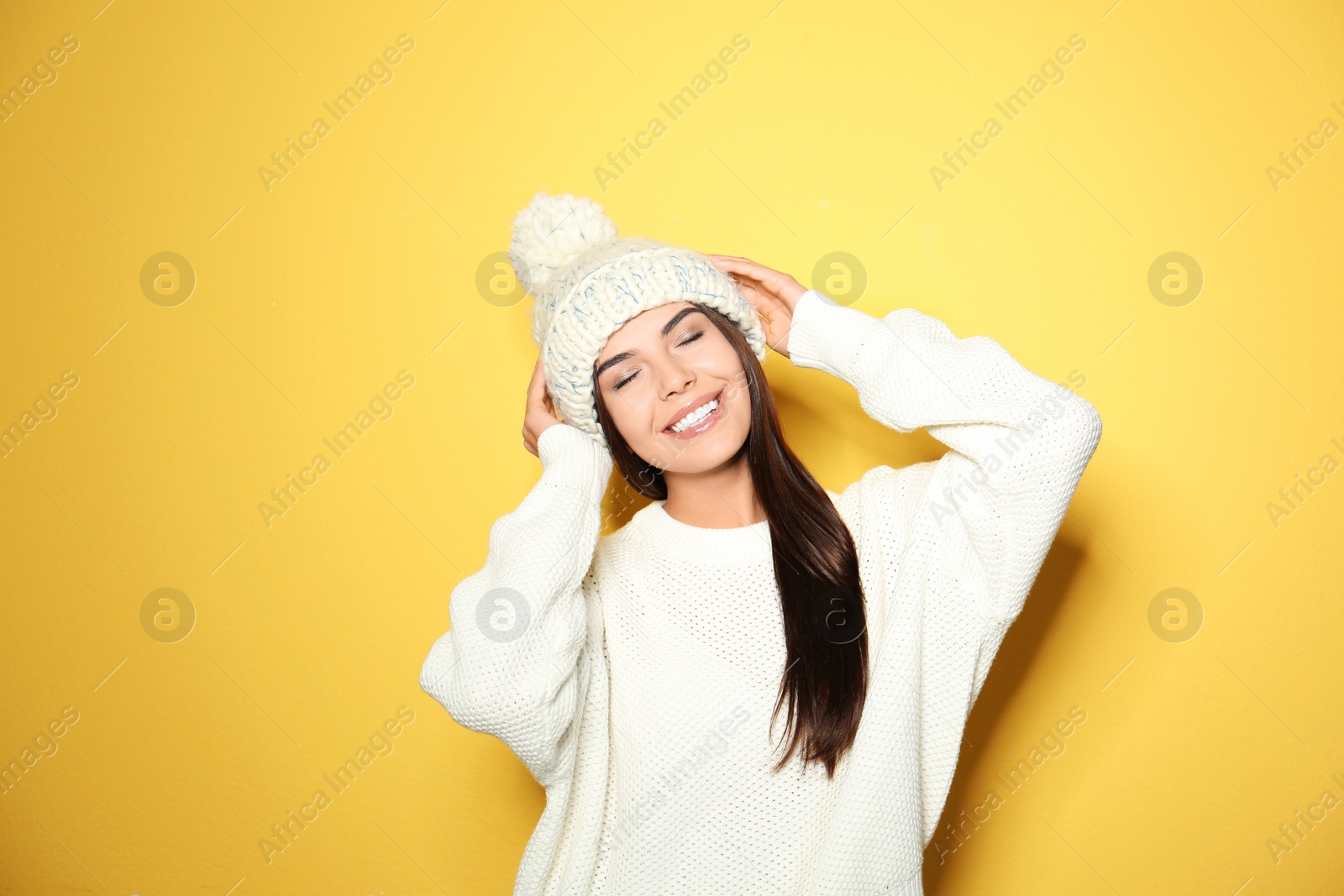 Image of Happy young woman wearing warm sweater and knitted hat on yellow background