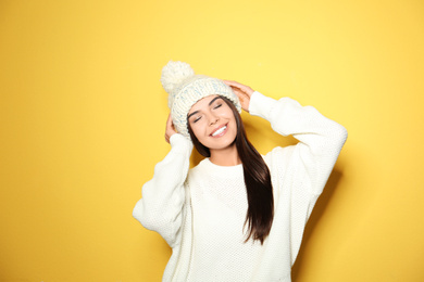 Image of Happy young woman wearing warm sweater and knitted hat on yellow background