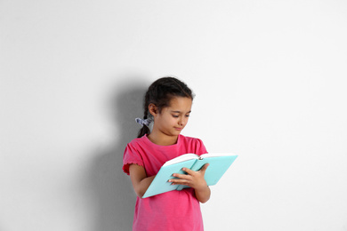 Cute little girl with book on light background