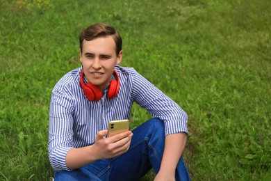 Photo of Handsome young man with headphones and smartphone on green grass outdoors