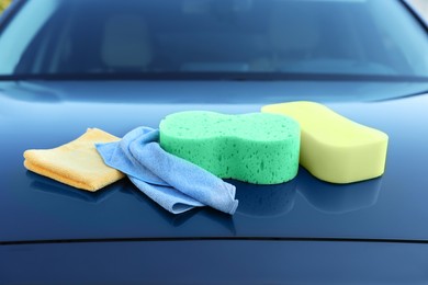 Photo of Sponges and rags on car hood outdoors. Cleaning products