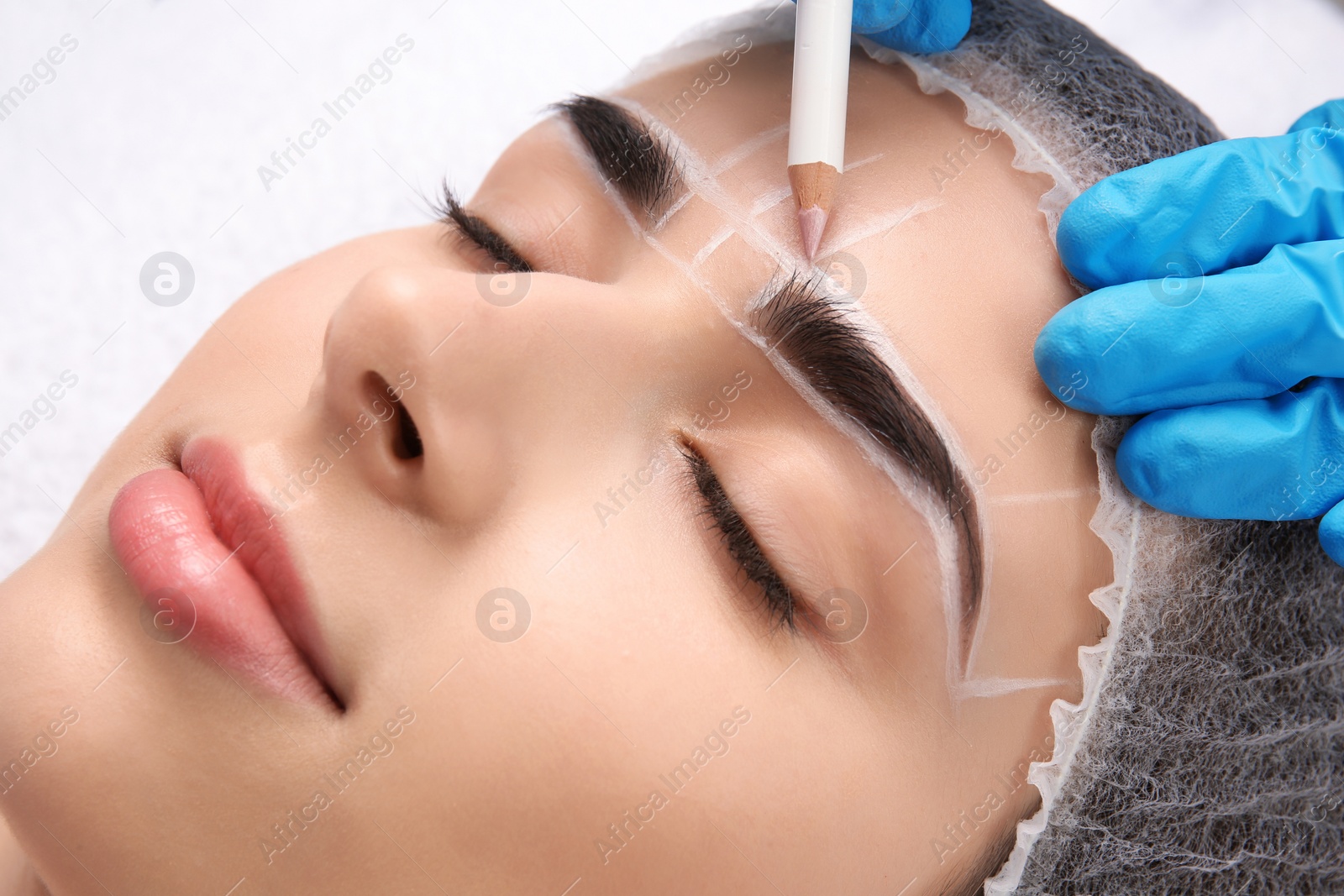 Photo of Cosmetologist preparing young woman for eyebrow permanent makeup procedure, closeup