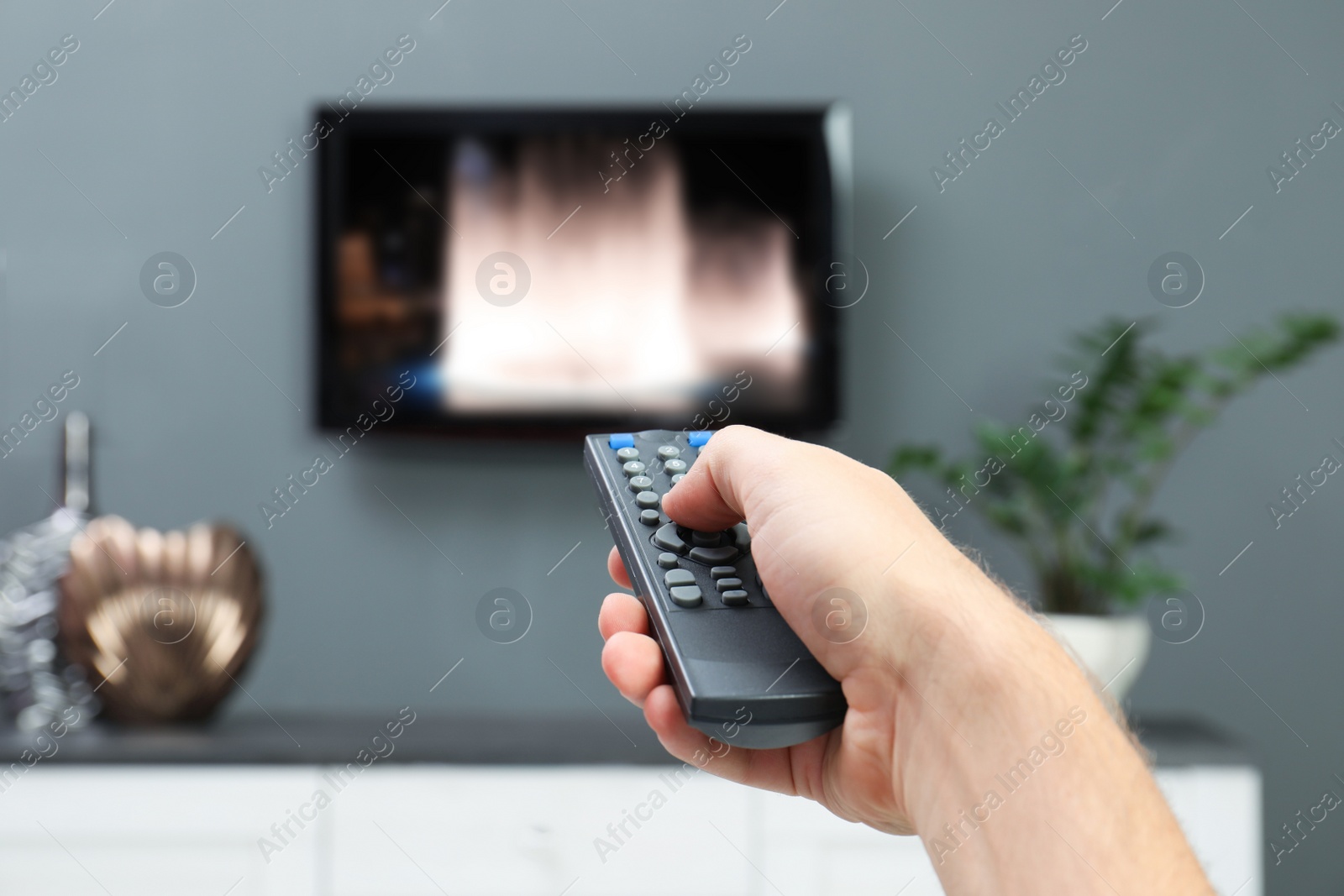 Image of Man switching channels on TV set with remote control at home