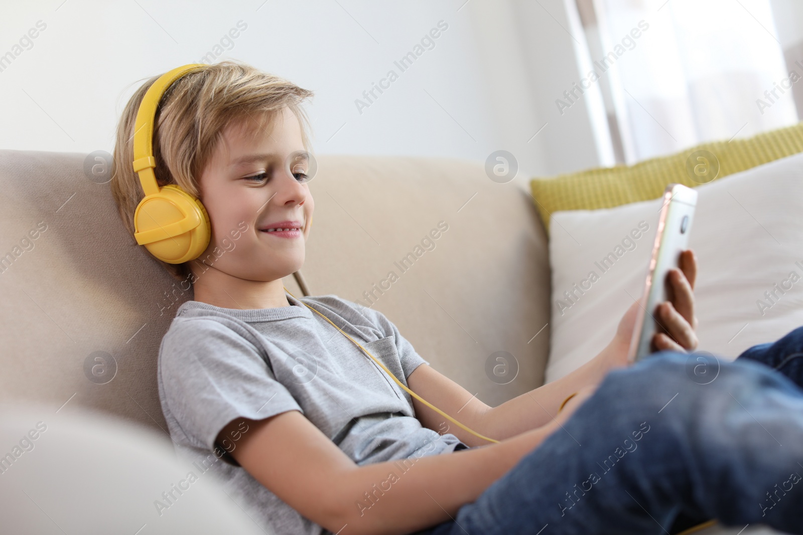 Photo of Cute little boy with headphones and smartphone listening to audiobook at home