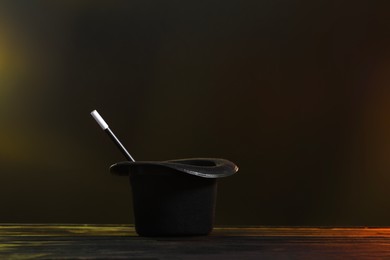 Photo of Magician's hat and wand on wooden table against lamps and dark background, space for text