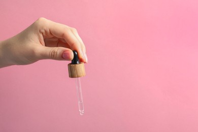 Woman holding pipette with serum against pink background, closeup. Space for text