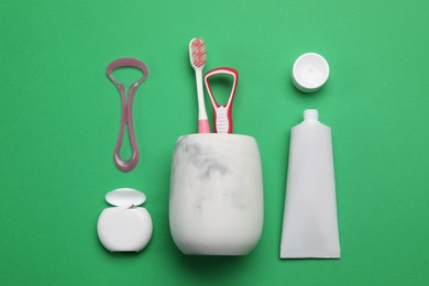 Photo of Flat lay composition with tongue cleaners and teeth care products on green background