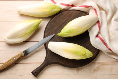 Photo of Raw ripe chicories and knife on wooden table, top view