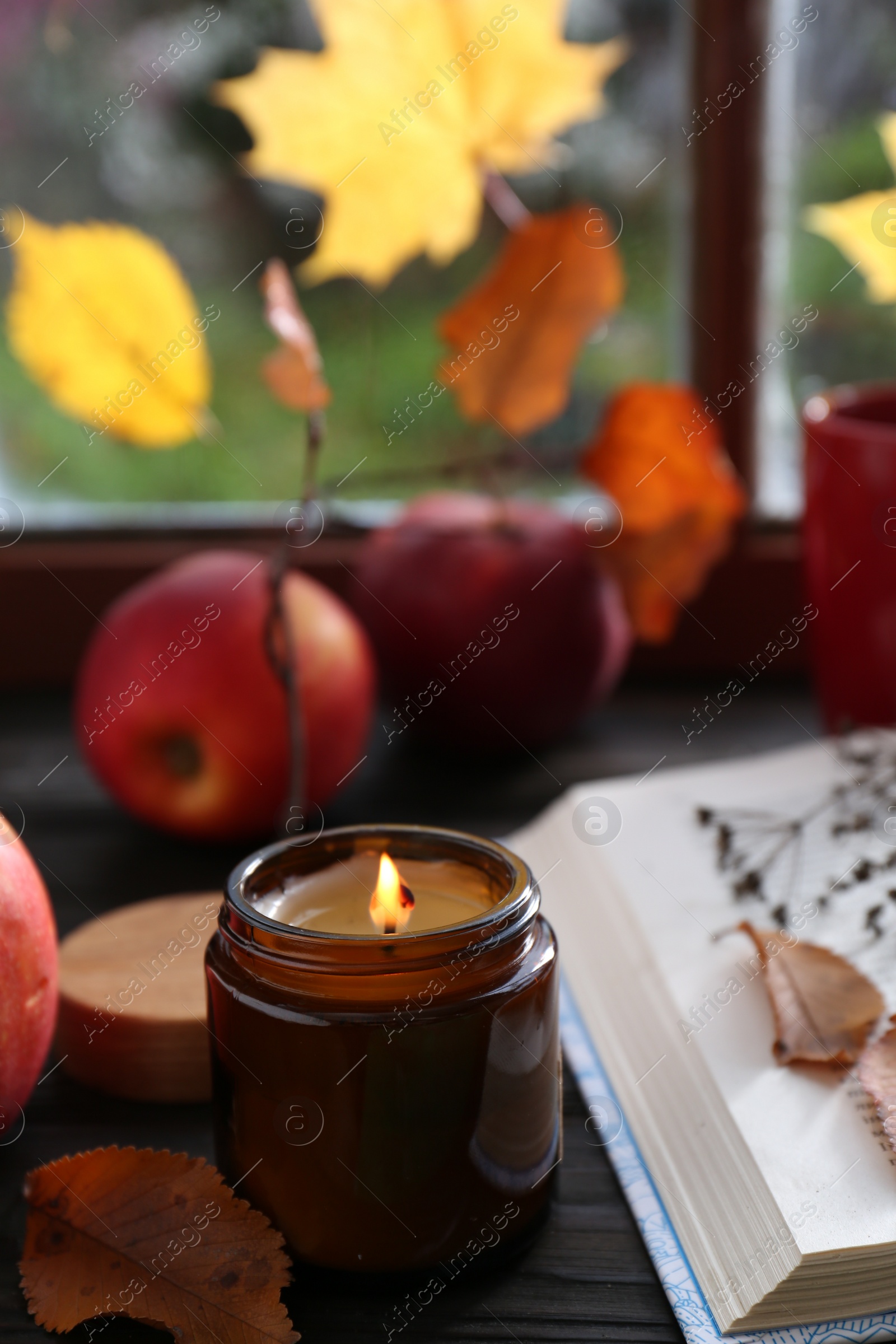 Photo of Beautiful burning candle and book on wooden table near window. Autumn atmosphere