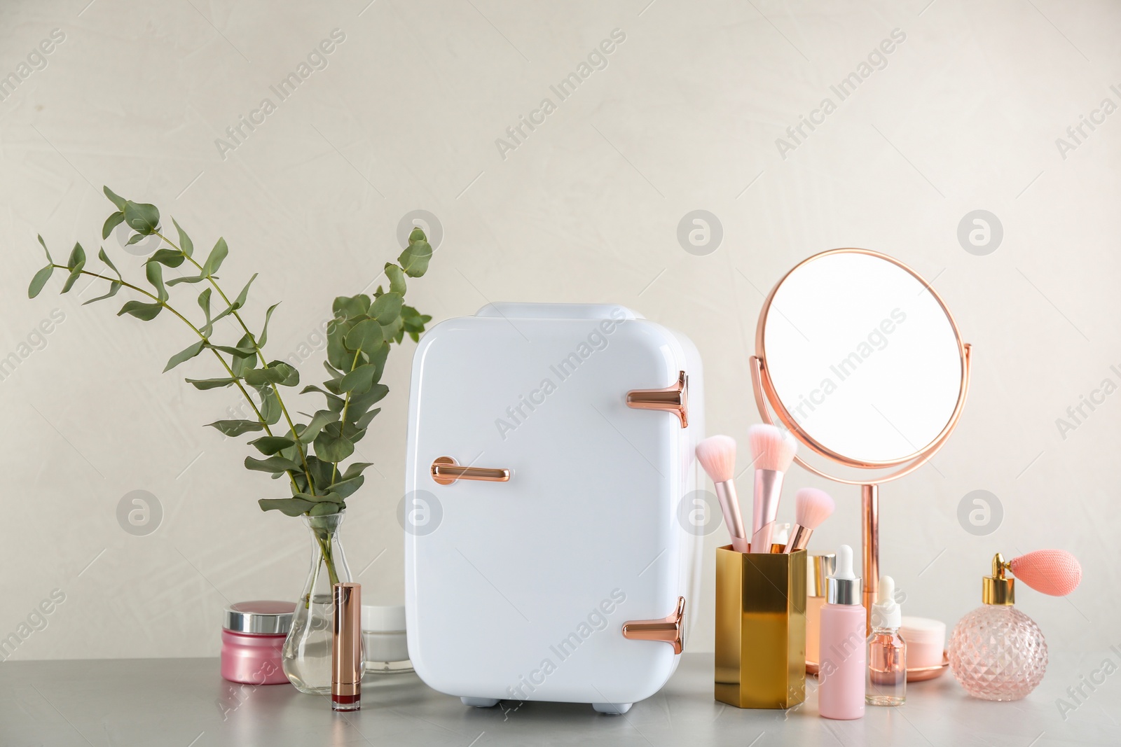 Photo of Cosmetic refrigerator and skin care products on beige background