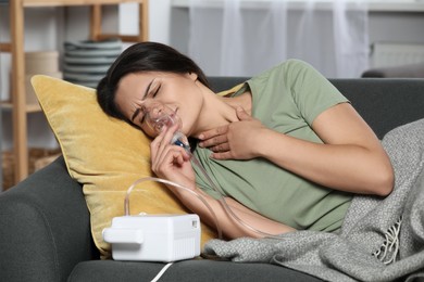 Photo of Sick young woman using nebulizer on couch at home