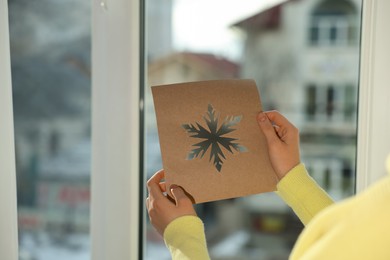 Photo of Woman holding snowflake stencil near window at home, closeup