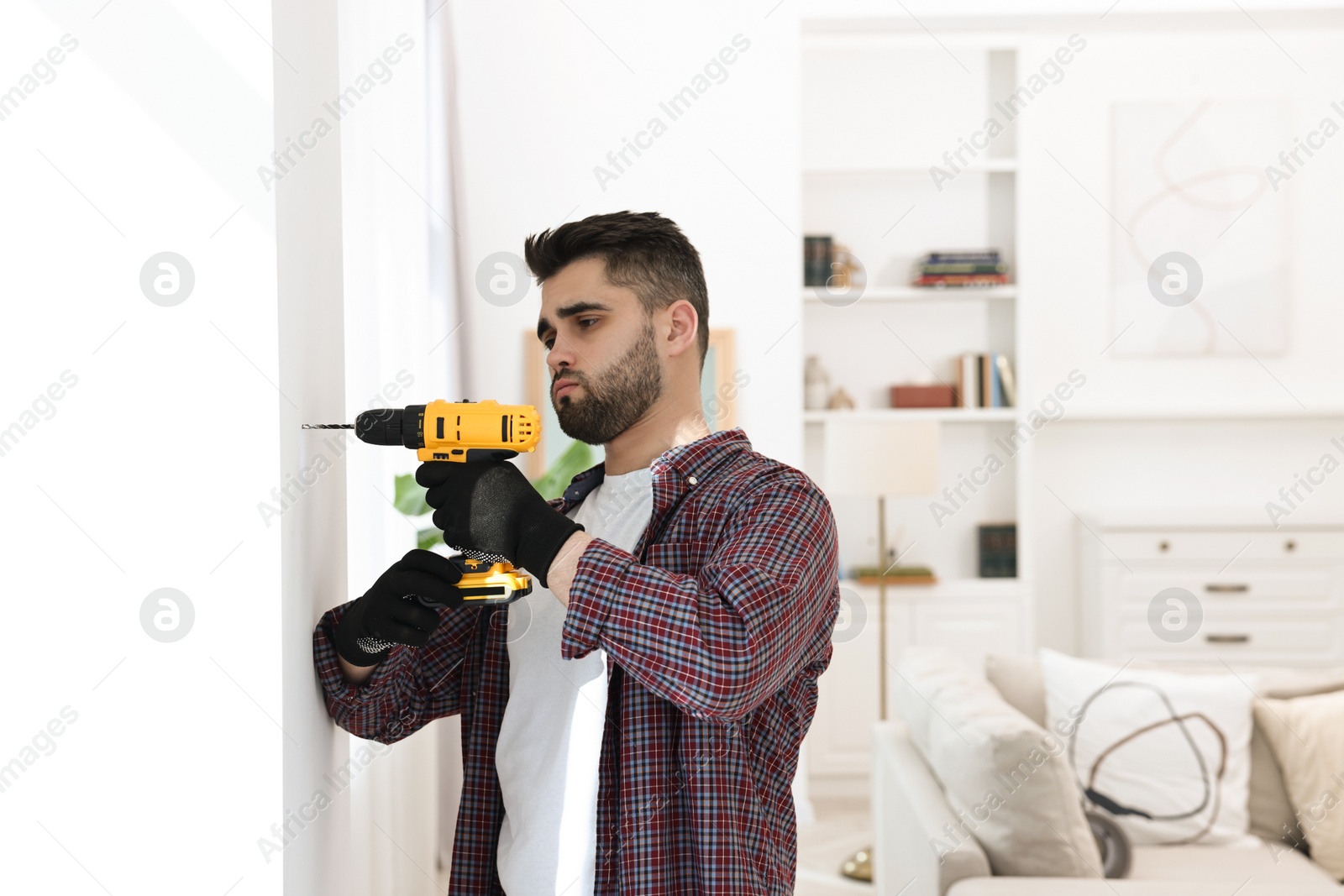 Photo of Young handyman working with electric drill at home