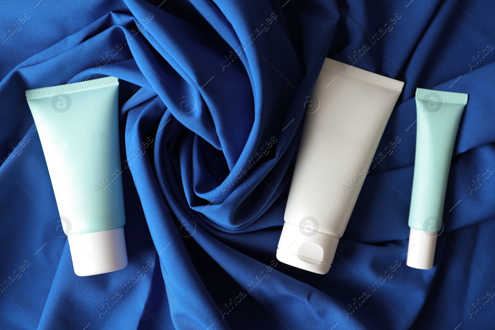 Photo of Set of luxury cosmetic products on blue fabric, flat lay