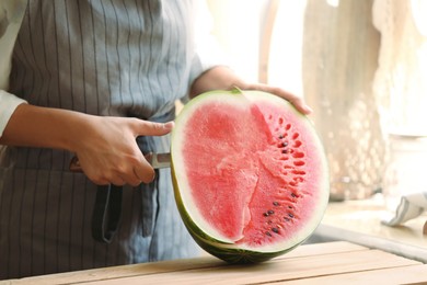 Woman cutting fresh juicy watermelon at wooden table, closeup