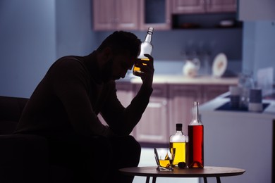 Image of Silhouette of addicted man with alcoholic drinks in kitchen