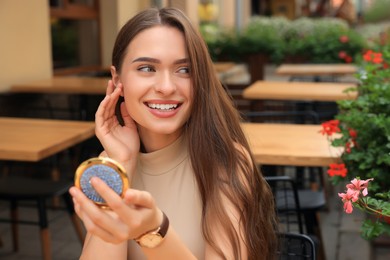 Photo of Beautiful young woman with cosmetic pocket mirror in outdoor cafe, space for text