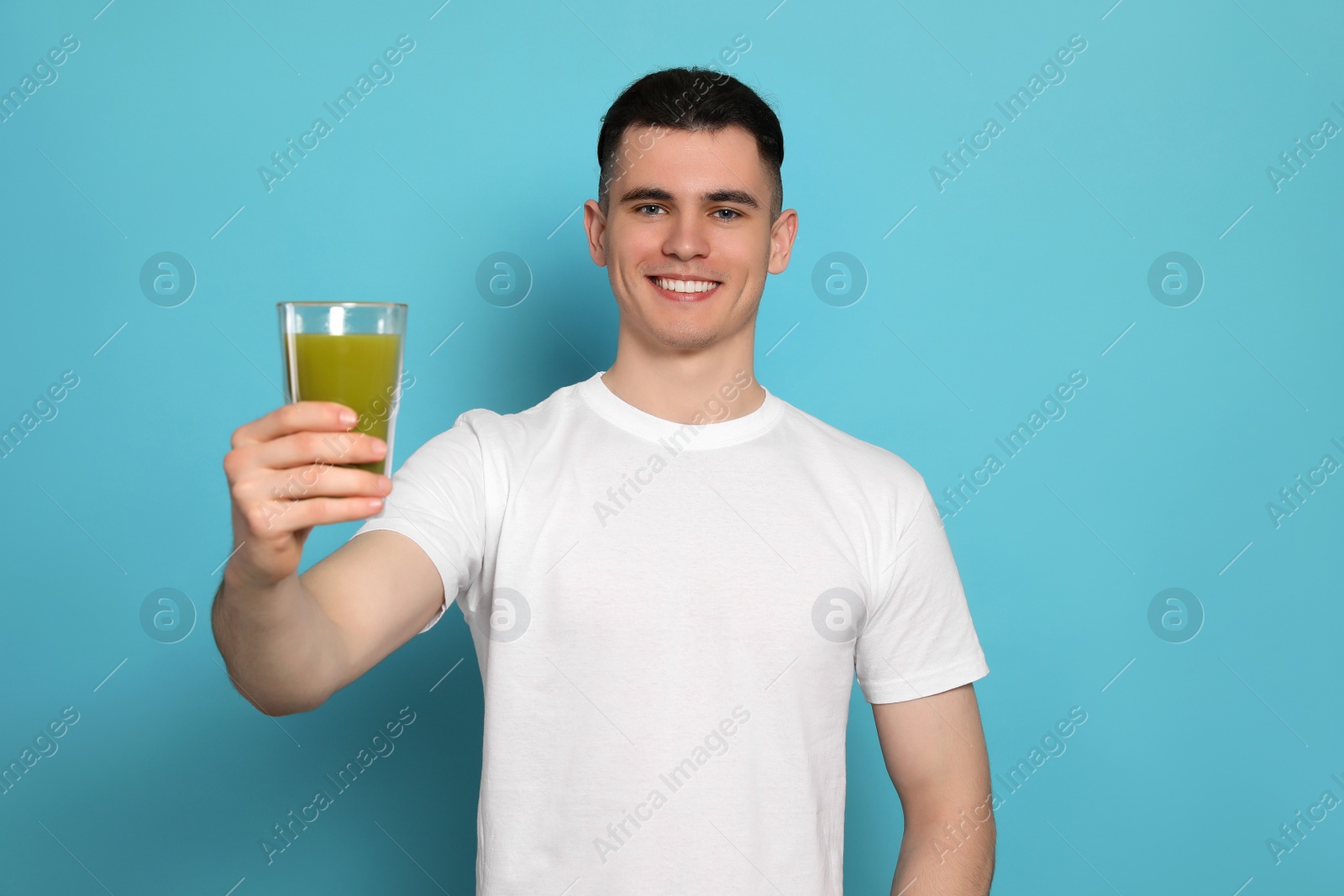 Photo of Handsome young man with glass of juice on light blue background