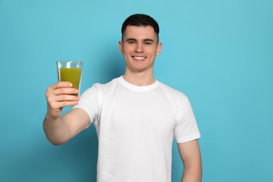 Photo of Handsome young man with glass of juice on light blue background