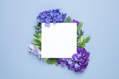 Photo of Beautiful composition with hortensia flowers and blank card on light blue background, top view. Space for text