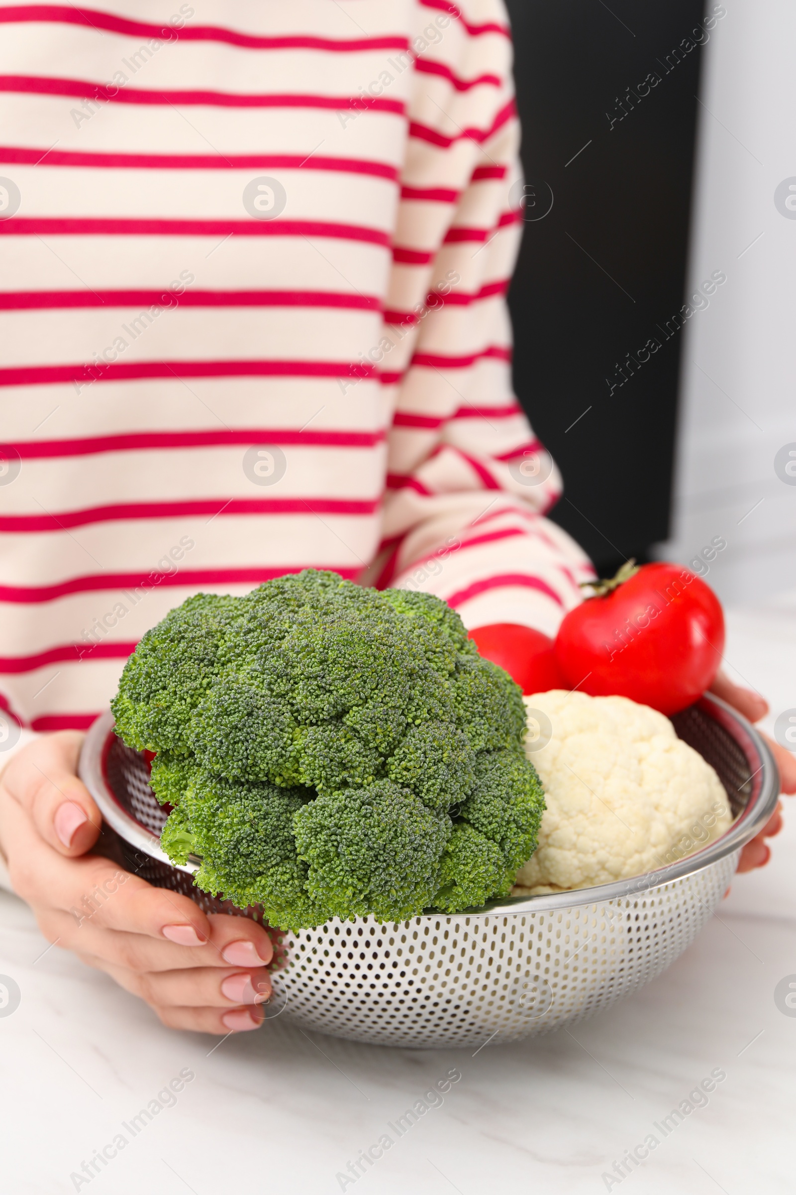 Photo of Woman holding colander with fresh vegetables at white marble table, closeup